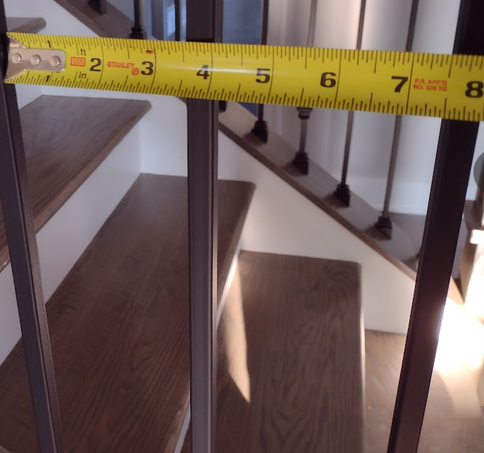 Measuring stair guard spacing with tape measure to verify code compliance with 43/8-inch maximum opening per IRC 2021.
