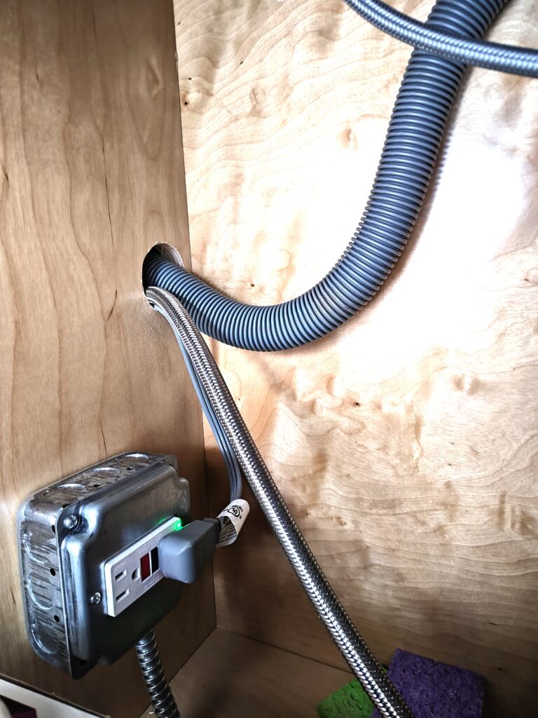 Close-up of a GFCI outlet with test and reset buttons, powering a dishwasher under a kitchen sink, demonstrating 2023 NEC GFCI protection requirement.