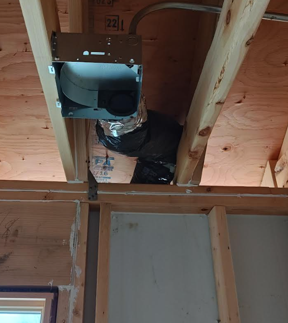 Bathroom exhaust fan housing installed between ceiling joists. Metal duct connected to fan, with UL 181–listed flex duct running toward exterior wall, shown before drywall installation. Example of code-compliant duct material for residential bathroom exhaust.