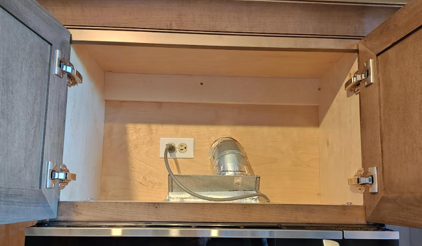 Kitchen cabinet above range hood showing accessible receptacle outlet for cord-and-plug connected appliance as required by NEC 422.16(B)(4).
