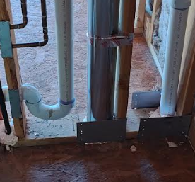 Dryer vent duct running through framing members with steel shield plates installed for nail protection, as required when ducts are within 1-1/4 inches of finished framing surfaces.