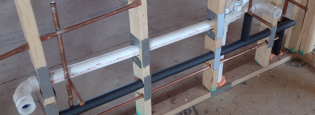 Drilled or notched studs with metal reinforcement and protective plates around plumbing penetrations